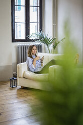 Woman relaxing on couch at home drinking coffee - GIOF03609