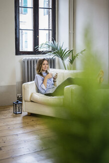 Frau entspannt sich auf der Couch zu Hause und trinkt Kaffee - GIOF03609