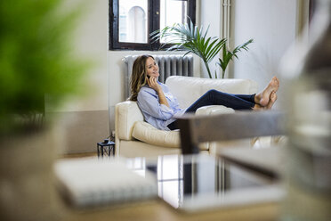 Smiling woman on couch at home on the phone - GIOF03612