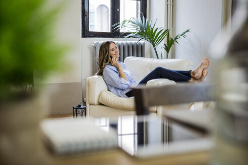 Lächelnde Frau auf der Couch zu Hause beim Telefonieren - GIOF03612