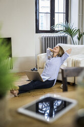 Smiling woman with laptop at home leaning back - GIOF03617