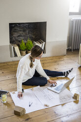 Woman sitting on the floor with blueprint and laptop - GIOF03620