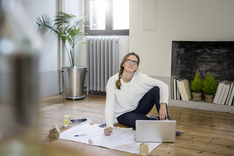 Frau sitzt mit Blaupause und Laptop auf dem Boden, lizenzfreies Stockfoto