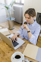 Woman using laptop on wooden desk at home - GIOF03631
