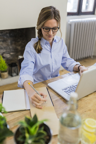 Frau benutzt Laptop und macht sich Notizen auf einem Holztisch zu Hause, lizenzfreies Stockfoto