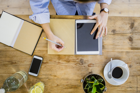 Top view of woman at wooden desk with notebook, cell phone and tablet stock photo