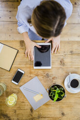 Draufsicht auf eine Frau an einem hölzernen Schreibtisch mit Notebook, Mobiltelefon und Tablet - GIOF03639