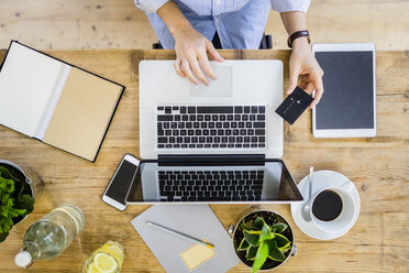 Top view of woman at wooden desk with credit card and laptop - GIOF03640