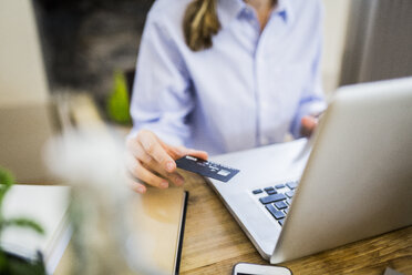 Close-up of woman at wooden desk with credit card and laptop - GIOF03642