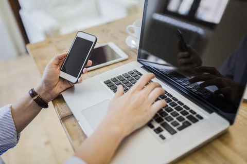 Close-up of woman at wooden desk with cell phone and laptop stock photo