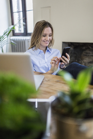 Smiling woman sitting at desk at home checking cell phone stock photo