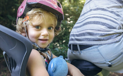 Porträt eines kleinen Mädchens mit Helm, das mit seinem Vater auf einem Kindersitz für ein Fahrrad sitzt - DAPF00827