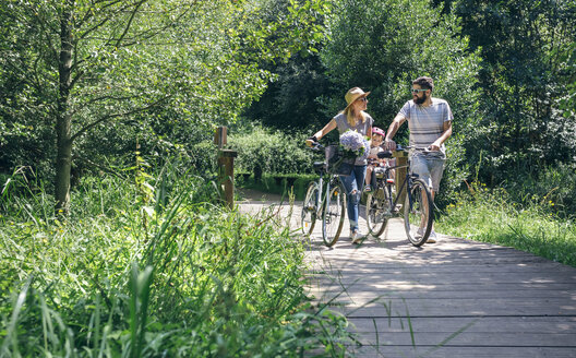 Family pushing bicycles on wooden walkway - DAPF00832