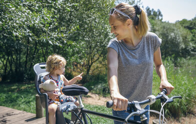 Mutter, die mit ihrer Tochter in einem Kindersitz eine Fahrradtour durch die Landschaft macht - DAPF00837