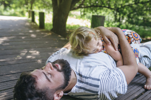 Little girl hugging her father lying on a wooden walkway in the countryside stock photo