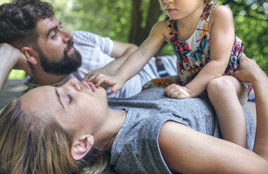 Little girl playing with her parents lying on a wooden walkway in the countryside - DAPF00845