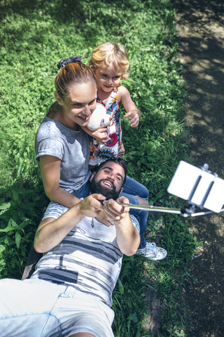 Glücklicher Mann, der auf einer Bank liegt und ein Selfie mit seiner Familie macht, lizenzfreies Stockfoto