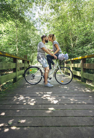 Paar mit Fahrrad küsst sich auf einem Holzsteg auf dem Lande, lizenzfreies Stockfoto