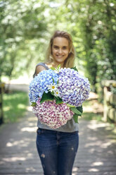Lächelnde junge Frau mit einem Blumenstrauß aus Hortensien und Gänseblümchen - DAPF00860