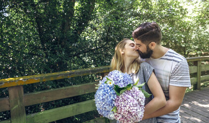 Paar mit einem Strauß Hortensien küsst sich auf einem Holzsteg auf dem Lande - DAPF00863