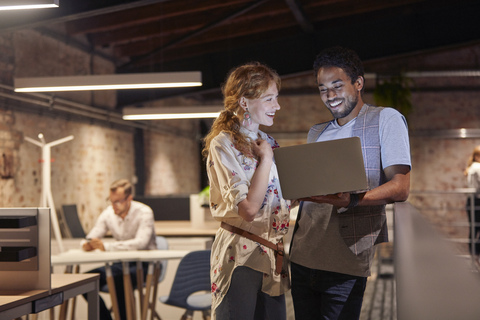 Man in office holding laptop, talking to colleague stock photo