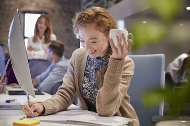 Junge Frau arbeitet in einem modernen, kreativen Büro und hält eine Tasse Kaffee - WESTF23810