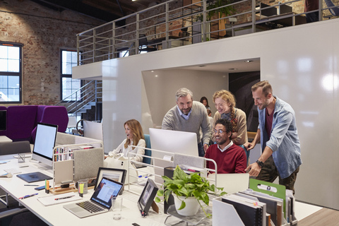 Colleagues looking over shoulder of young man working in modern office stock photo