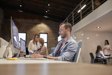 Man working at desk in office, smiling - WESTF23816