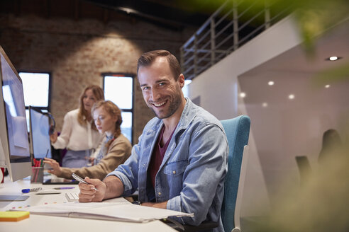 Man working at desk in office, smiling - WESTF23820