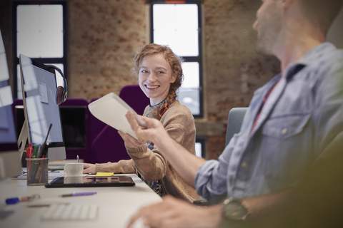 Young man helping colleague sitting at desk in office, smiling stock photo