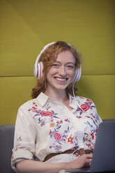 Junge Frau arbeitet in einem modernen, kreativen Büro und trägt Kopfhörer - WESTF23830