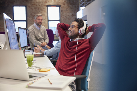 Young man sitting at desk in office, wearing headphones, smiling stock photo