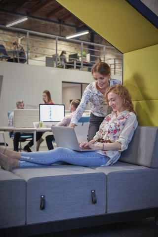 Junge Frau arbeitet in einem modernen, kreativen Büro und benutzt einen Laptop, lizenzfreies Stockfoto