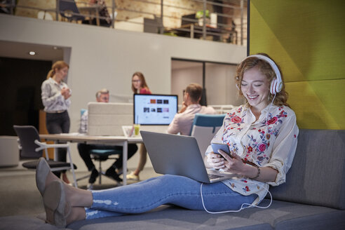 Young woman working in modern creative office, usine laptop and headphones - WESTF23855