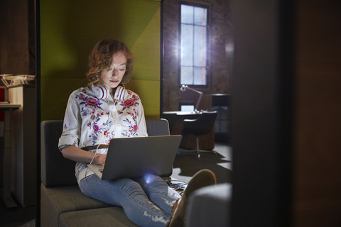 Junge Frau sitzt auf der Couch und arbeitet am Laptop, lizenzfreies Stockfoto