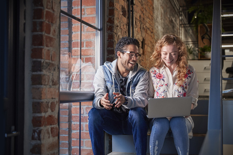 Young business people sitting on stairs in loft office using laptop stock photo