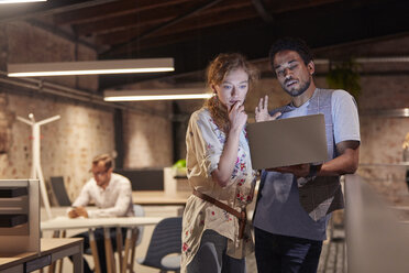 Man in office holding laptop, talking to colleague - WESTF23869