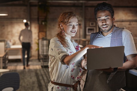 Man in office holding laptop, talking to colleague stock photo