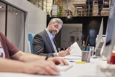 Businessman sitting at desk in office, looking curious stock photo