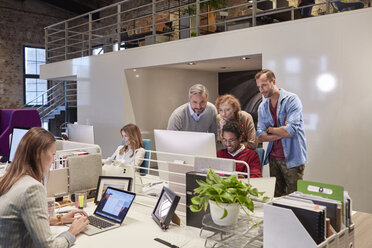 Colleagues looking over shoulder of young man working in modern office - WESTF23881