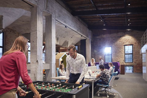 Business people in office taking a break, playing foosball stock photo