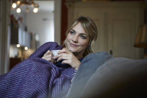 Portrait of smiling woman with cup of tea relaxing on couch at home stock photo