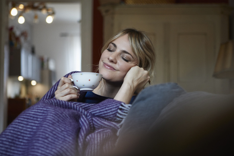 Portrait of smiling woman with cup of tea relaxing on couch at home stock photo