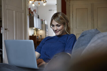 Porträt einer lächelnden Frau mit Laptop auf der Couch zu Hause - RBF06174