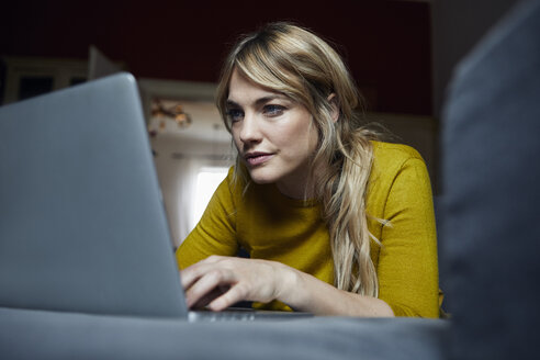 Porträt einer Frau, die zu Hause auf der Couch liegt und einen Laptop benutzt - RBF06179