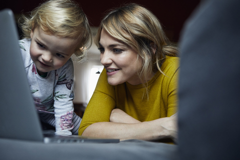 Porträt von Mutter und kleiner Tochter, die zu Hause auf einen Laptop schauen, lizenzfreies Stockfoto