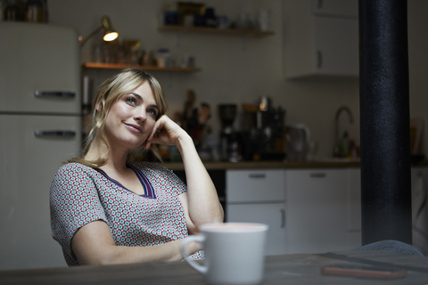 Porträt einer träumenden Frau, die in der Küche am Tisch sitzt, lizenzfreies Stockfoto