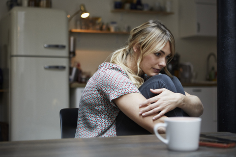 Portrait of pensive woman sitting at table in the kitchen stock photo