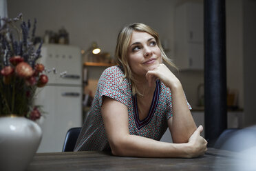 Portrait of smiling woman sitting at table in the kitchen thinking - RBF06196