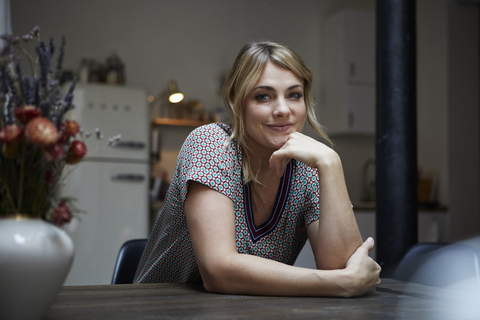 Portrait of smiling woman sitting at table in the kitchen stock photo